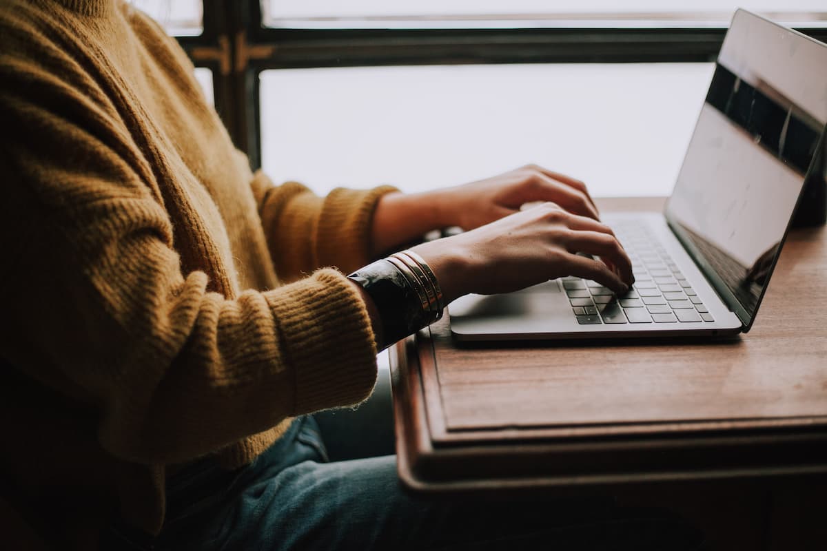 Man wearing a sweater and sitting at a desk while typing on his computer.